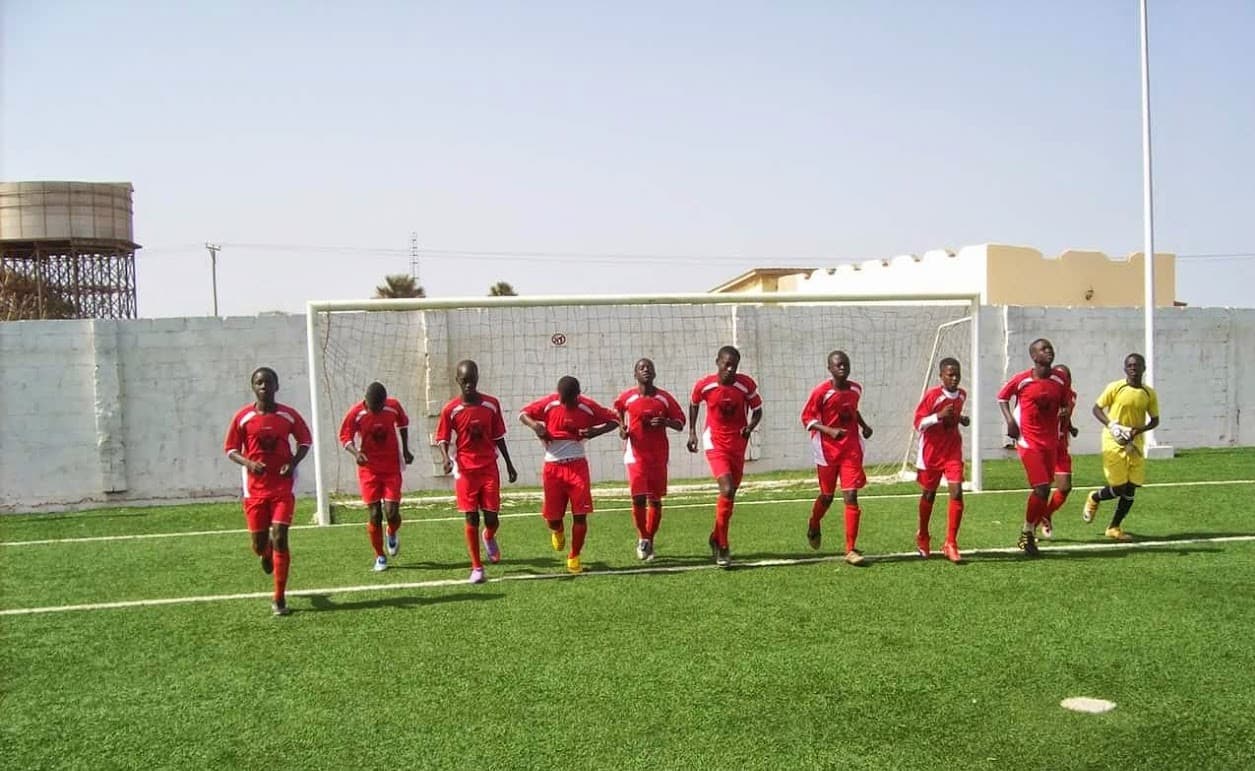 Young academy players in red kit warming up together on the pitch